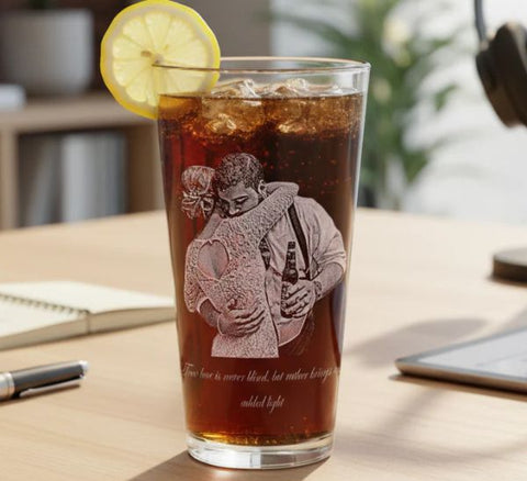 Personalized photo pint glass etched with a couple embracing, filled with iced cola and a lemon slice, on a desk beside a notebook and laptop