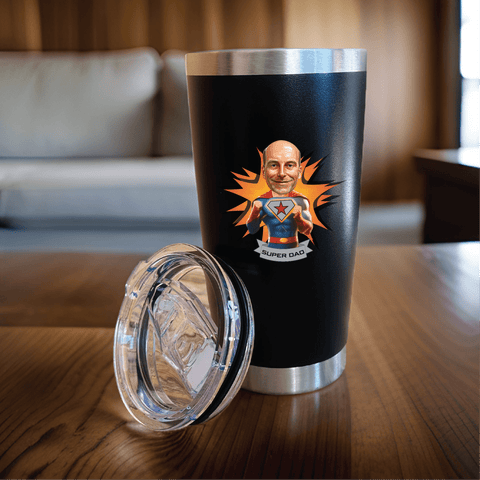 Personalized black stainless tumbler printed with a custom superhero caricature and Super Dad text, shown with its clear lid on a wooden table.