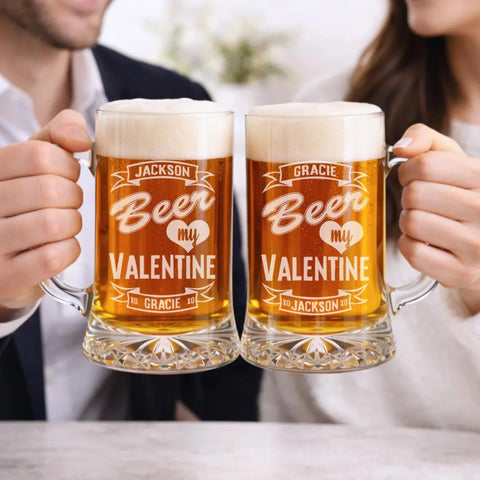 Couple holding personalized beer mugs with sample names and "Beer My Valentine" engraving, filled with beer and topped with foam.