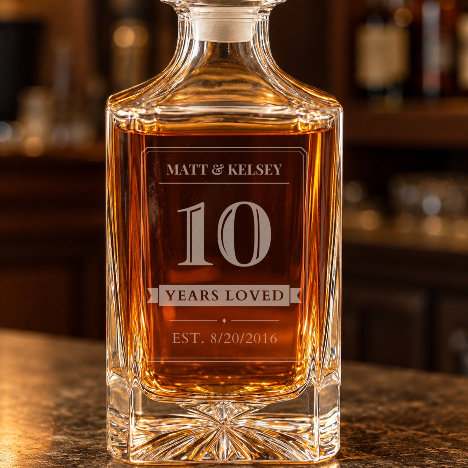 Close-up of the frosted laser engraving on a 10 year anniversary whiskey decanter: Matt and Kelsey, a bold 10, a Years Loved ribbon and EST. 8/20/2016