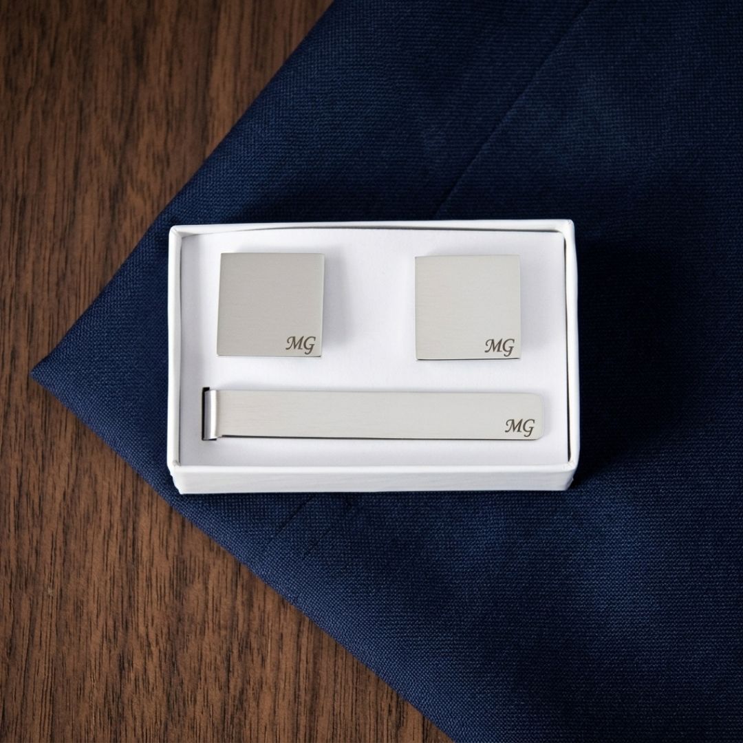 Three-piece cufflinks set in white gift box showing pair of square cufflinks and tie bar, each engraved with sample monogram "MG