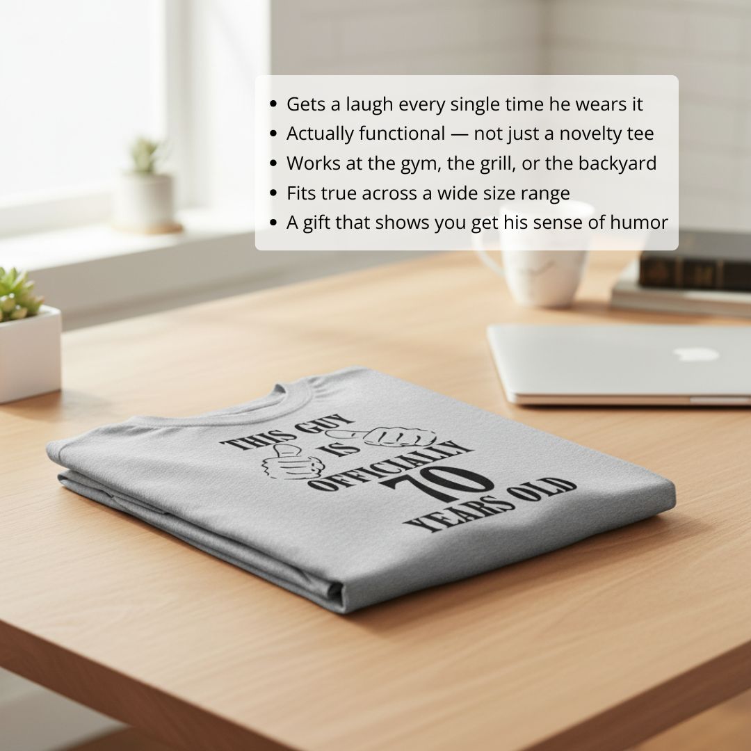Light grey unisex t-shirt folded on wooden desk, printed with bold text reading "This Guy is Officially 70 Years Old