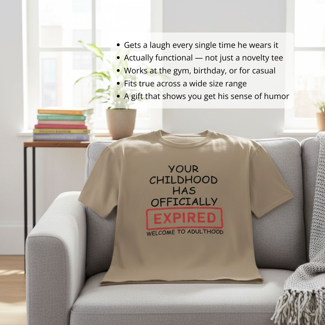 Tan t-shirt displayed on gray couch with printed text reading "YOUR CHILDHOOD HAS OFFICIALLY EXPIRED" with red stamp box and "WELCOME TO ADULTHOOD" below