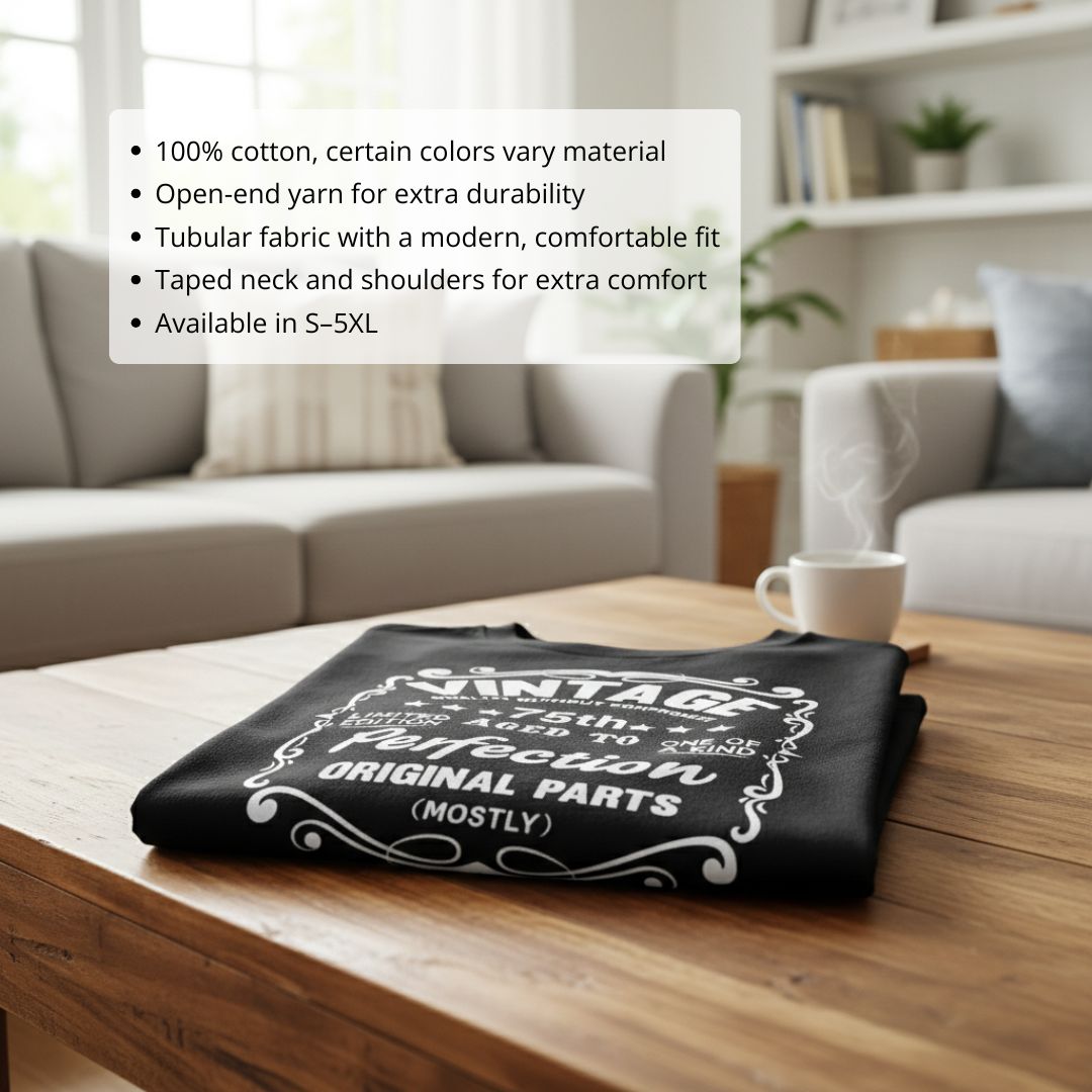 Black unisex t-shirt with white vintage-style graphic reading "Vintage" and "Original Parts (Mostly)" with decorative flourishes, displayed folded on wooden table