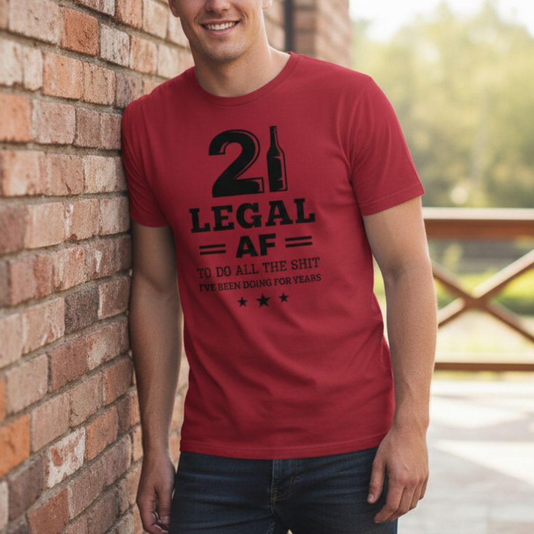 Red crewneck t-shirt with black graphic reading "21 LEGAL AF" with wine bottle icon and text "TO DO ALL THE SHIT I'VE BEEN DOING FOR YEARS" with decorative stars