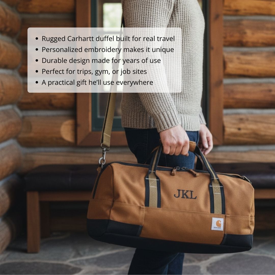 Tan and black Carhartt duffel bag with sample monogram "JKL" embroidered on front, carried by person in beige sweater against log cabin backdrop
