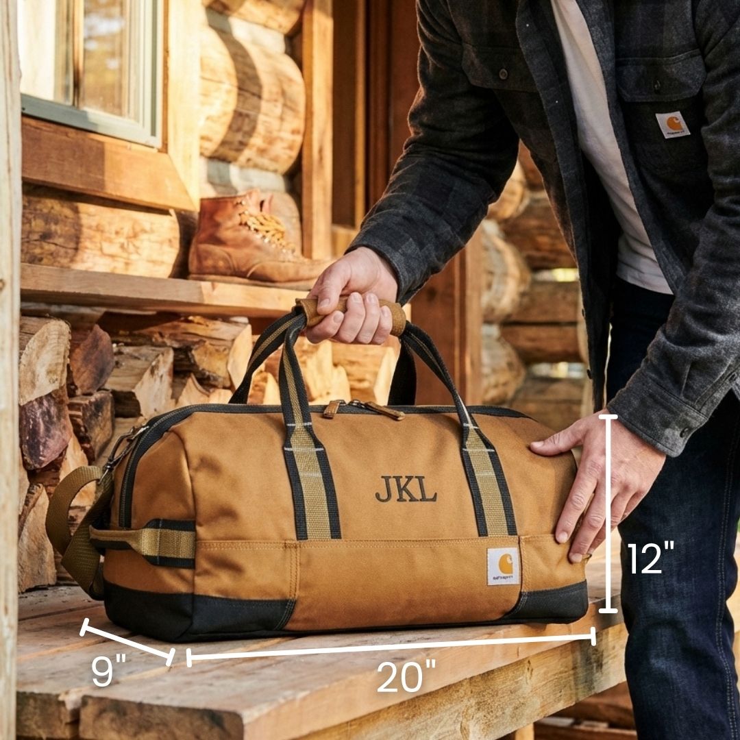 Tan canvas duffel bag with black straps, monogrammed with sample initials "JKL", displayed with dimensions 20" × 12" × 9" in rustic wood setting.