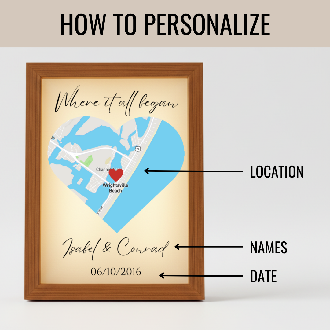 Framed map art with heart-shaped design showing sample location marker, text reading "Where it all began" at top, names "Isabel & Conrad" and date "06/10/2016" at bottom, demonstrating personalization options