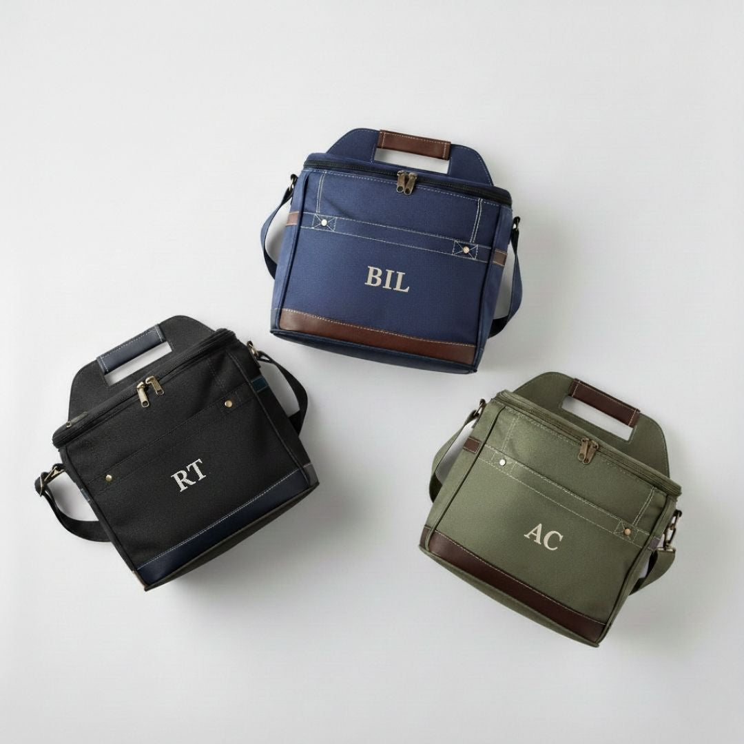 Three personalized cooler bags displayed in navy with sample monogram "BIL", black with "RT", and olive green with "AC", each featuring brown leather trim and shoulder straps