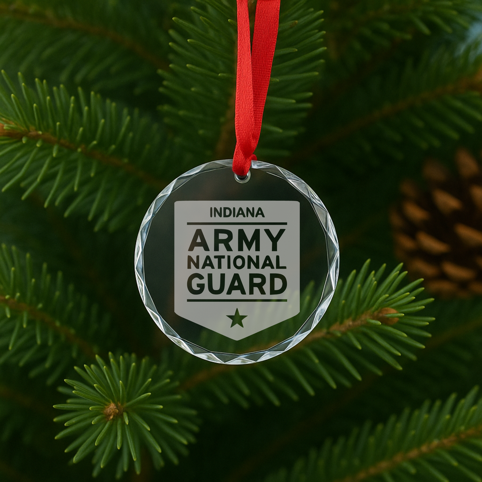 Round faceted glass ornament with red ribbon, engraved with Indiana Army National Guard logo and shield design on evergreen branch background