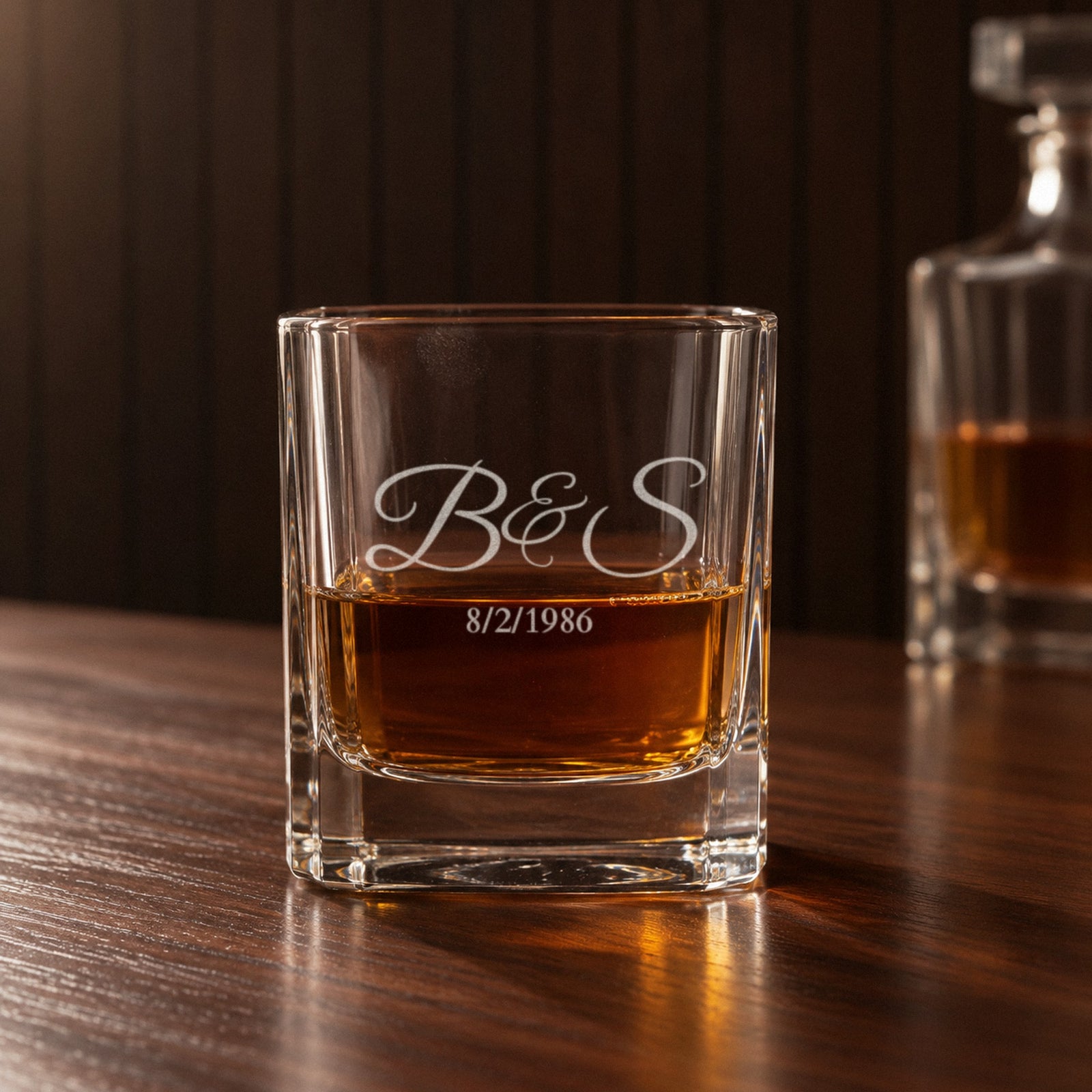 Close-up of an engraved rocks glass from the personalized whiskey decanter set, frosted initials B&S and the date 8/2/1986 with whiskey showing through