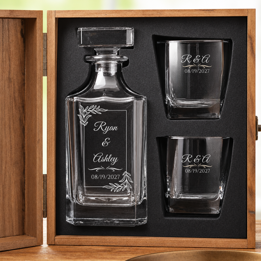 Open wooden gift box holding the 1 year anniversary decanter and two matching whiskey glasses, each engraved with the couple's names and anniversary date.