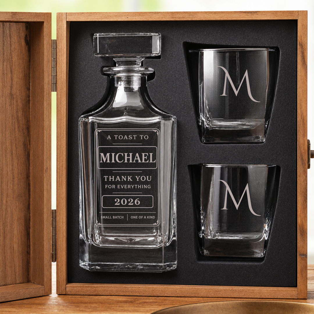Open pine chest holding a personalized thank you whiskey decanter engraved with a name and year, plus two crystal glasses each engraved with a single initial.