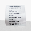 Care label on fabric showing washing instructions including machine wash delicate, do not bleach, tumble dry low heat, and laundry symbols.