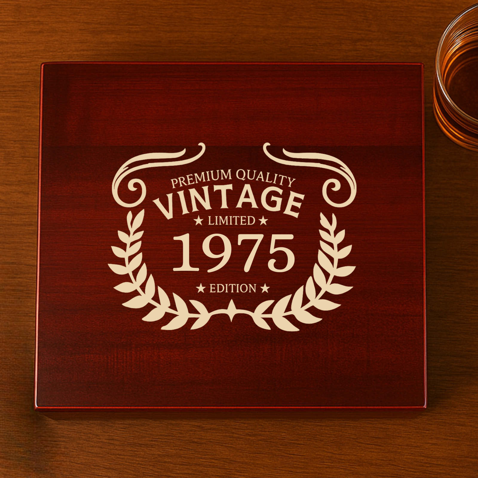 Burgundy keepsake box with cream engraving reading "Premium Quality Vintage Limited 1975 Edition" surrounded by laurel wreaths, displayed on wooden table with glass of whiskey