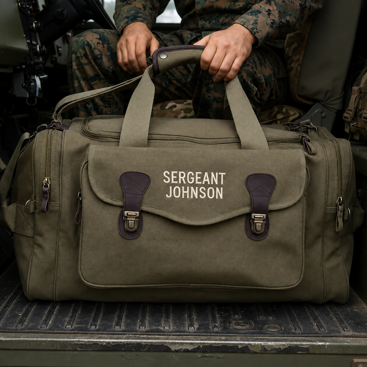 Olive canvas duffle bag with engraved sample text "SERGEANT JOHNSON" on front flap, held by person in military camouflage uniform