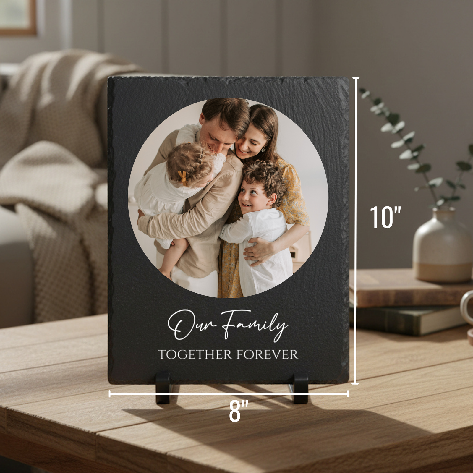 Black slate plaque with circular photo of family with two children, personalized with sample text "Our family Together Forever" displayed on wooden table with easel stand