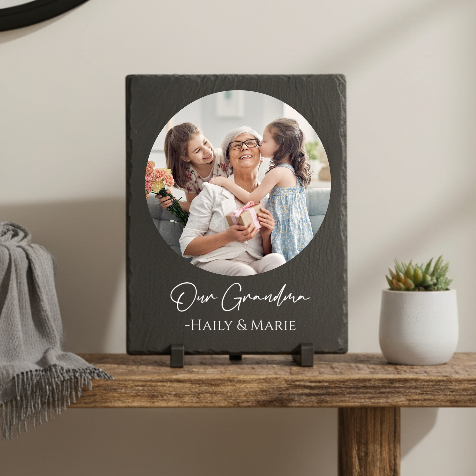 Dark slate plaque with circular photo cutout displaying grandmother with two granddaughters, engraved with sample text "Our Grandma -HAILY & MARIE" in script and block lettering