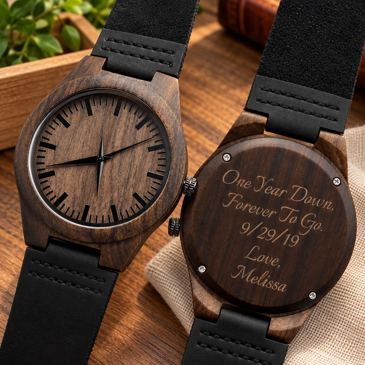 Two dark sandalwood watches on white marble, one face up showing the wood dial, one turned over showing an anniversary date and name engraved on the caseback