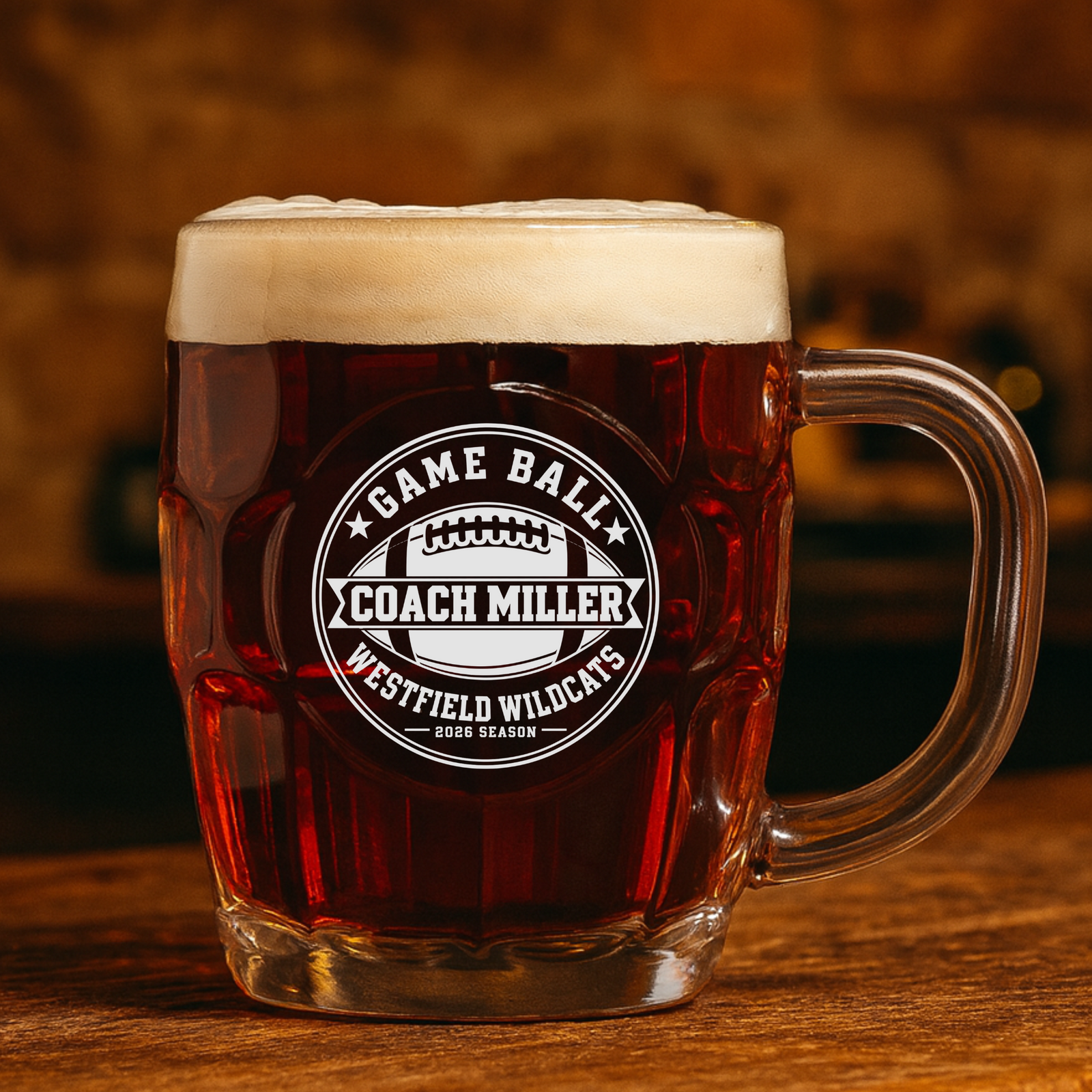 Custom football beer stein filled with dark amber ale on a rustic wooden bar, the Game Ball crest engraved with Coach Miller and Westfield Wildcats