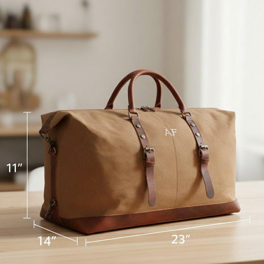 Tan waxed canvas travel bag with brown leather handles and trim, monogrammed with sample initials "AF" on front, displayed with dimension measurements 23" × 14" × 11