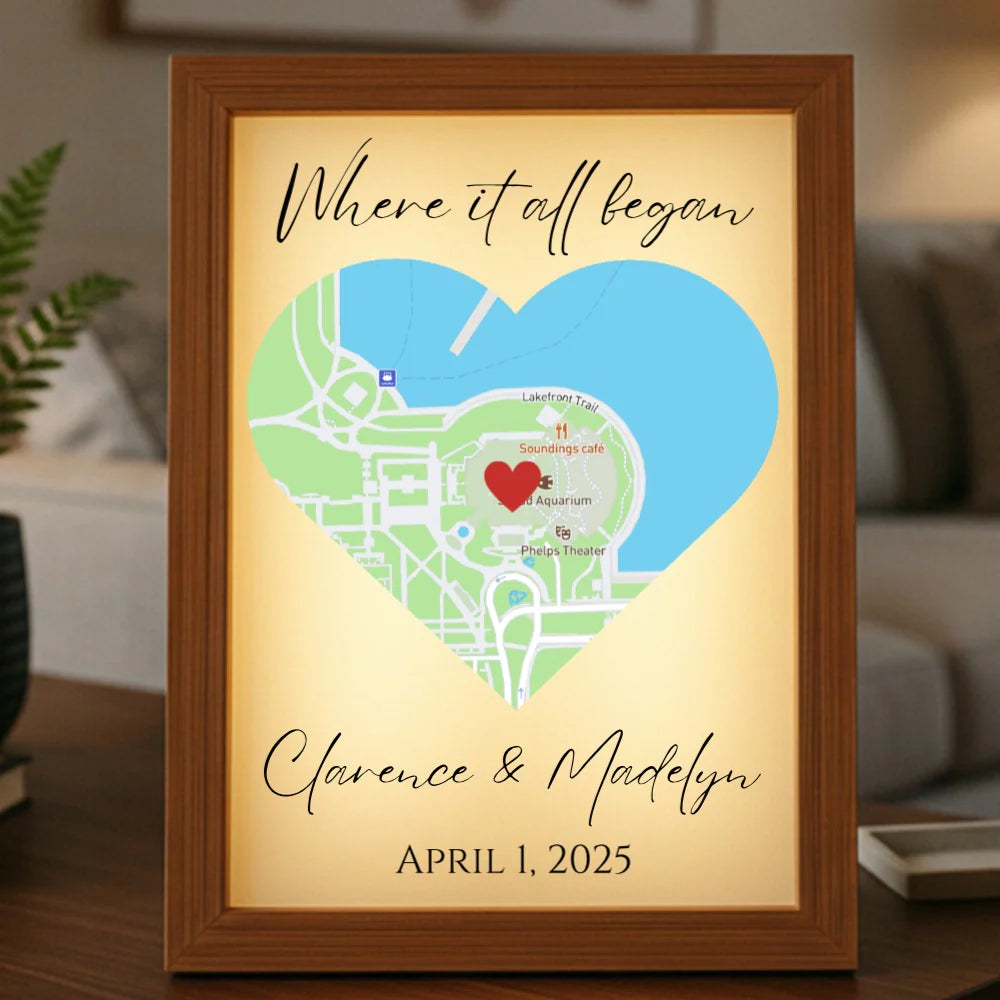 Framed light-up map art with personalized text "Where it all began," sample names "Clarence & Madelyn," date "April 1, 2025," red heart marker, and wood frame with LED illumination