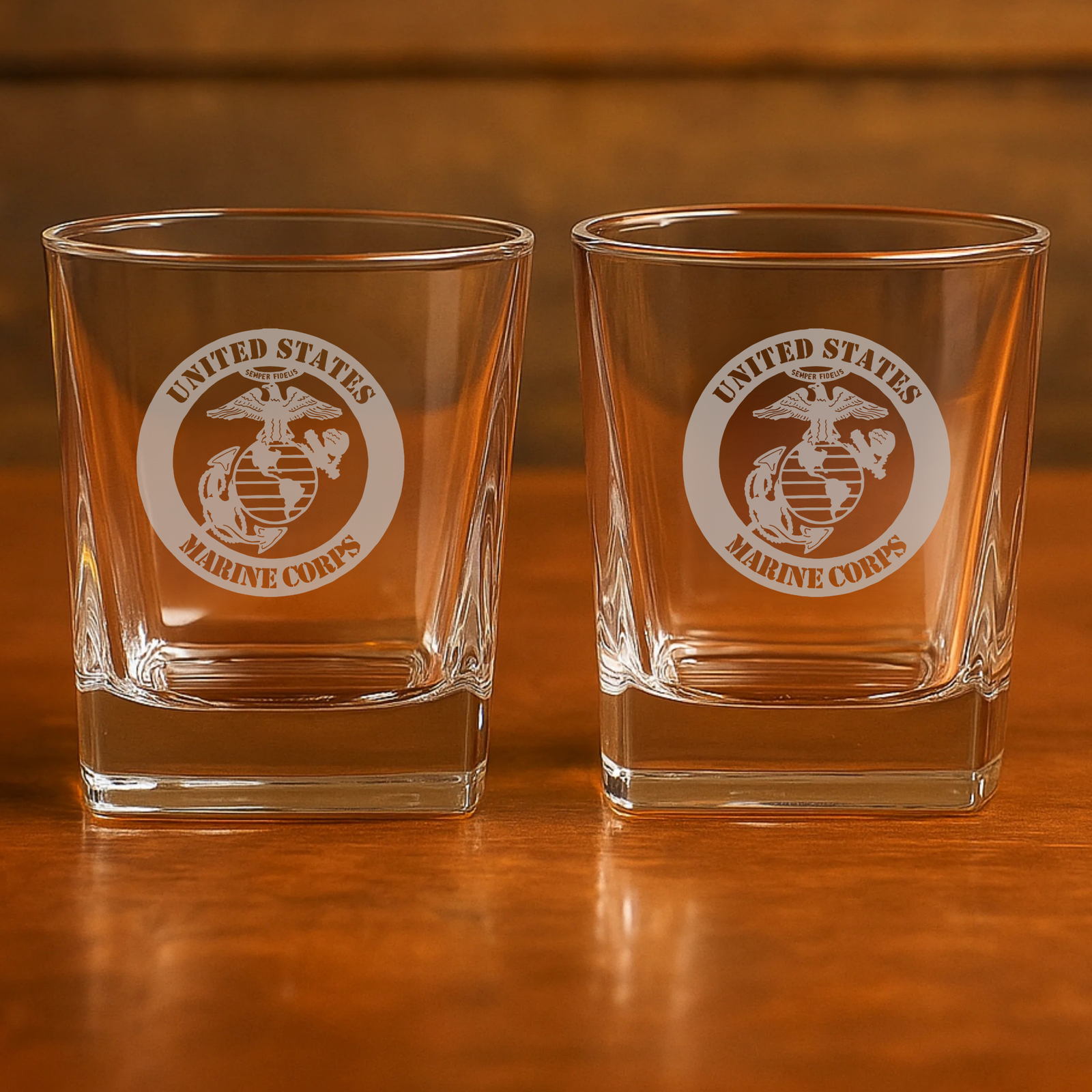 Two clear whiskey glasses with laser-engraved United States Marine Corps emblem and eagle logo, displayed side by side on wooden surface