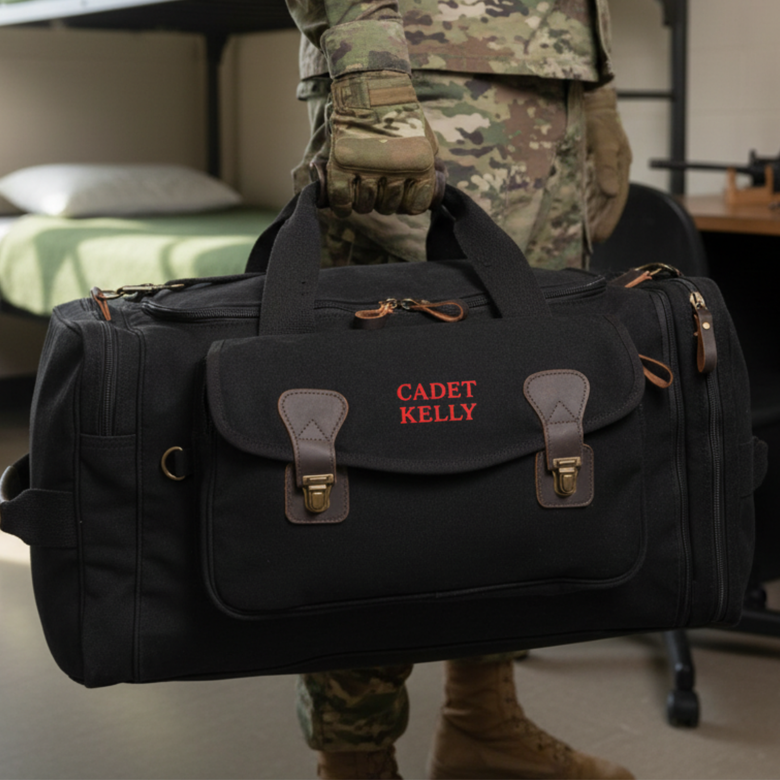 Black canvas duffel bag with brown leather handles and accents, personalized with sample embroidery "CADET KELLY" in red text on front flap