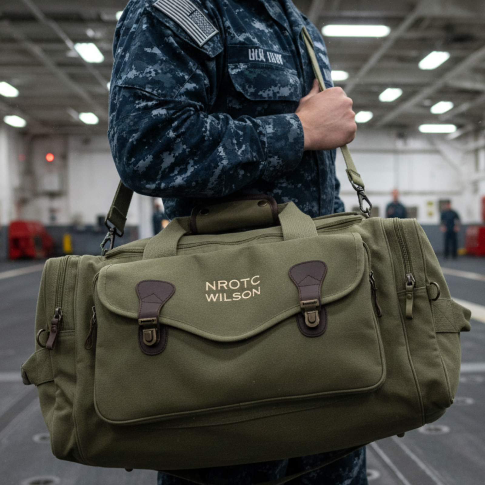 Olive canvas duffle bag with personalized embroidery reading "NROTC WILSON" worn over shoulder by person in Navy uniform indoors