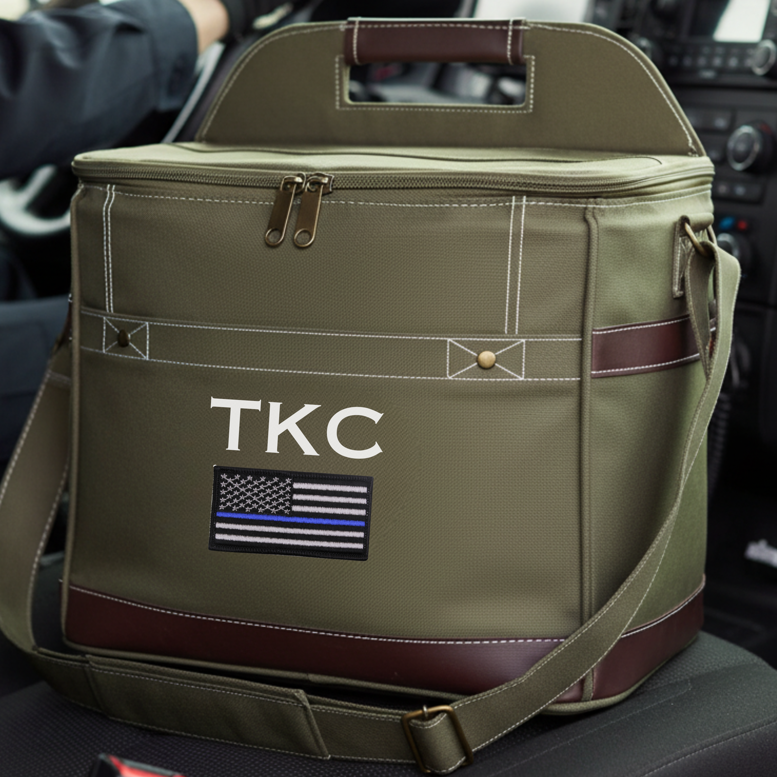 Sage green insulated cooler with brown leather trim, sample engraving "TKC" and thin blue line flag patch on front panel.