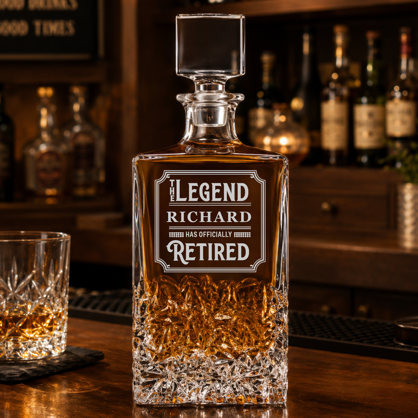 Crystal whiskey decanter with sample engraving reading "The Legend Richard Has Officially Retired" displayed on bar counter with matching glass