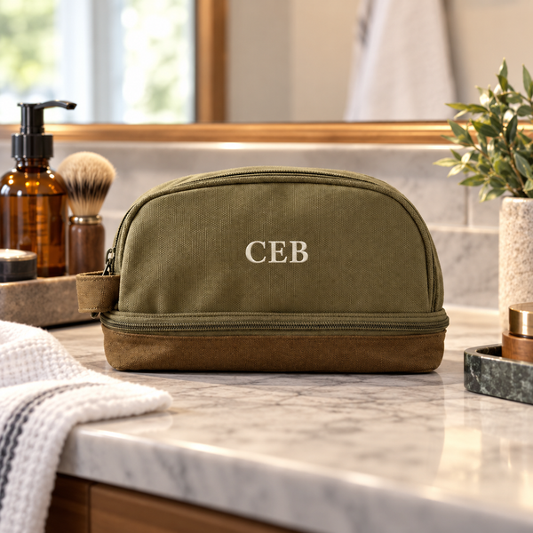 Personalized olive green canvas toiletry bag embroidered with the initials BIL in cream thread, standing on a bathroom vanity shelf