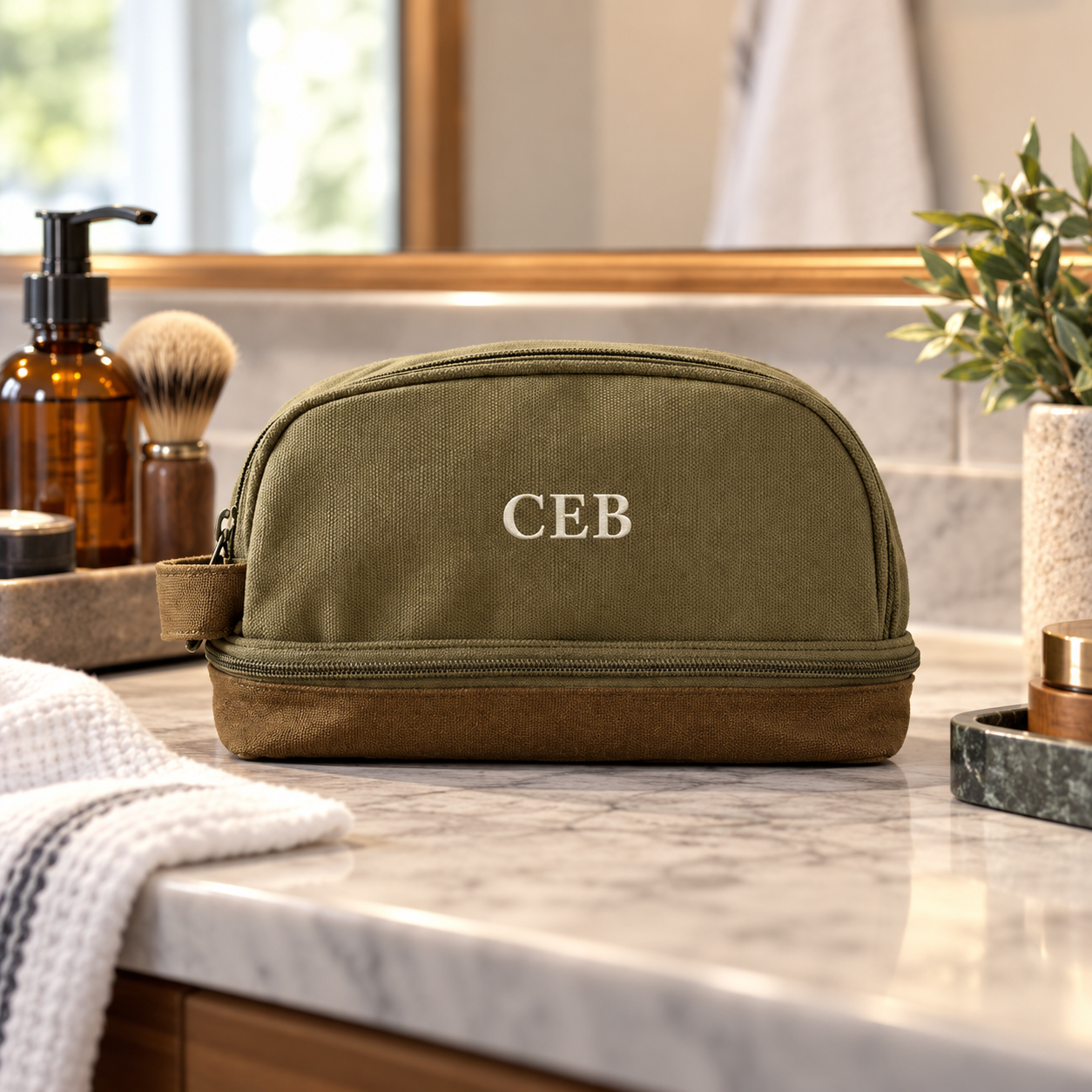 Personalized olive green canvas toiletry bag embroidered with the initials BIL in cream thread, standing on a bathroom vanity shelf