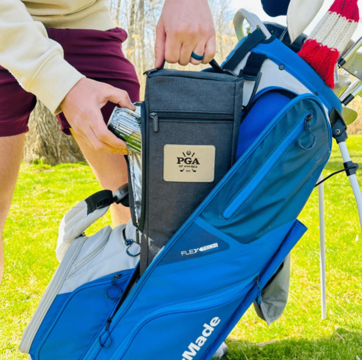 Golfer holding open gray and blue insulated cooler bag with PGA logo patch attached to golf bag on sunny course