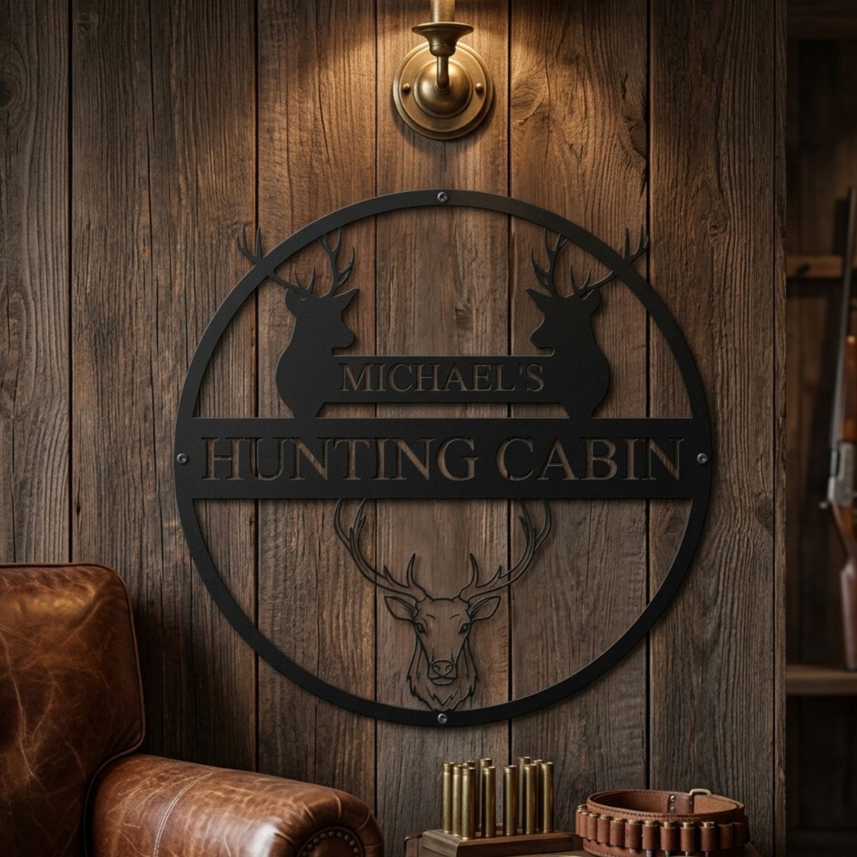 Black metal circular wall sign with deer head silhouettes and sample personalization reading "Michael's Hunting Cabin" mounted on wood paneling above leather chair and ammunition display.