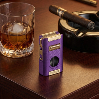 Purple torch lighter with gold accents displayed next to a whiskey glass with ice and cigar on wooden surface