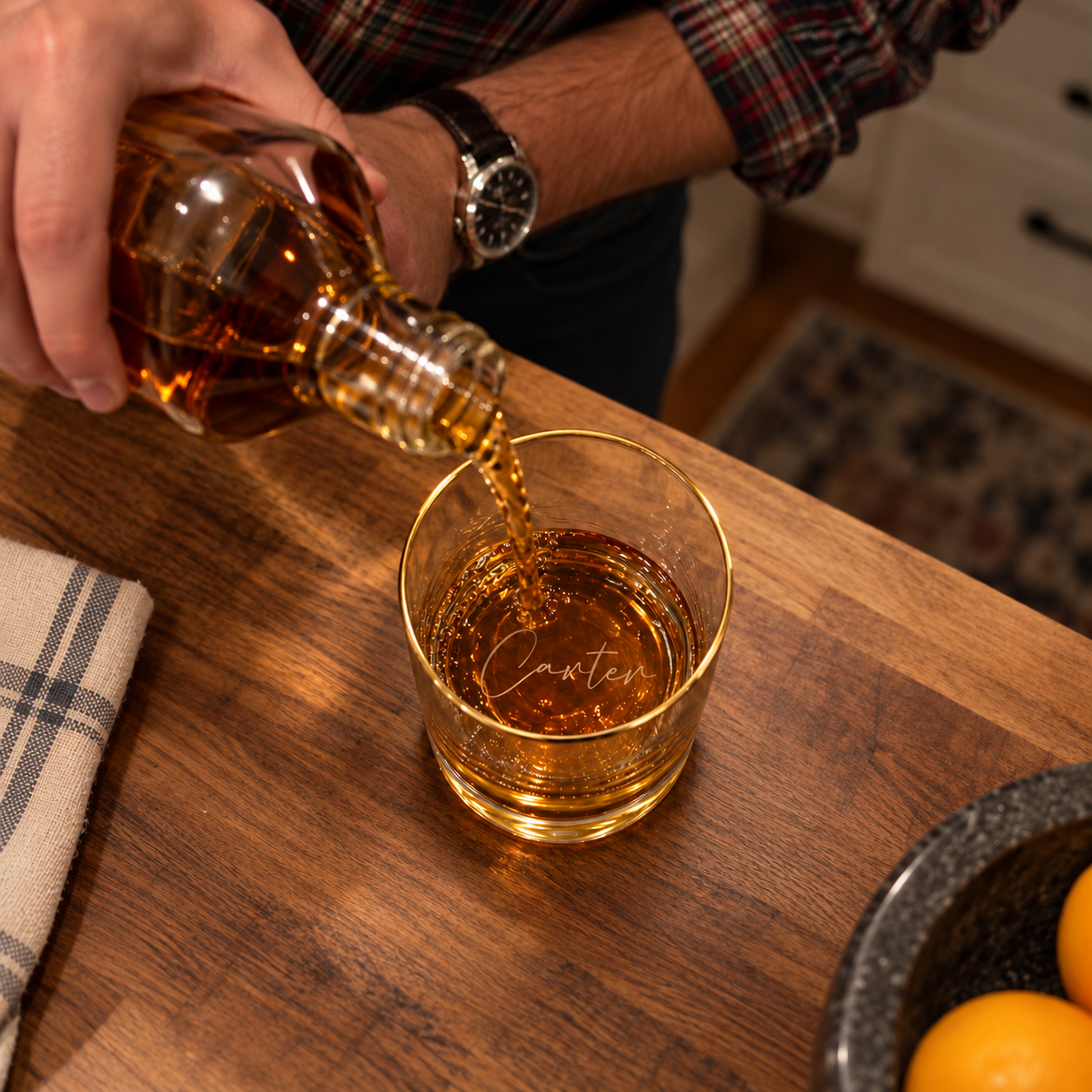 Hand pouring bourbon from a decanter into a gold rim whiskey glass with Carter engraved on the bottom, a thoughtful whisky glass gift for him