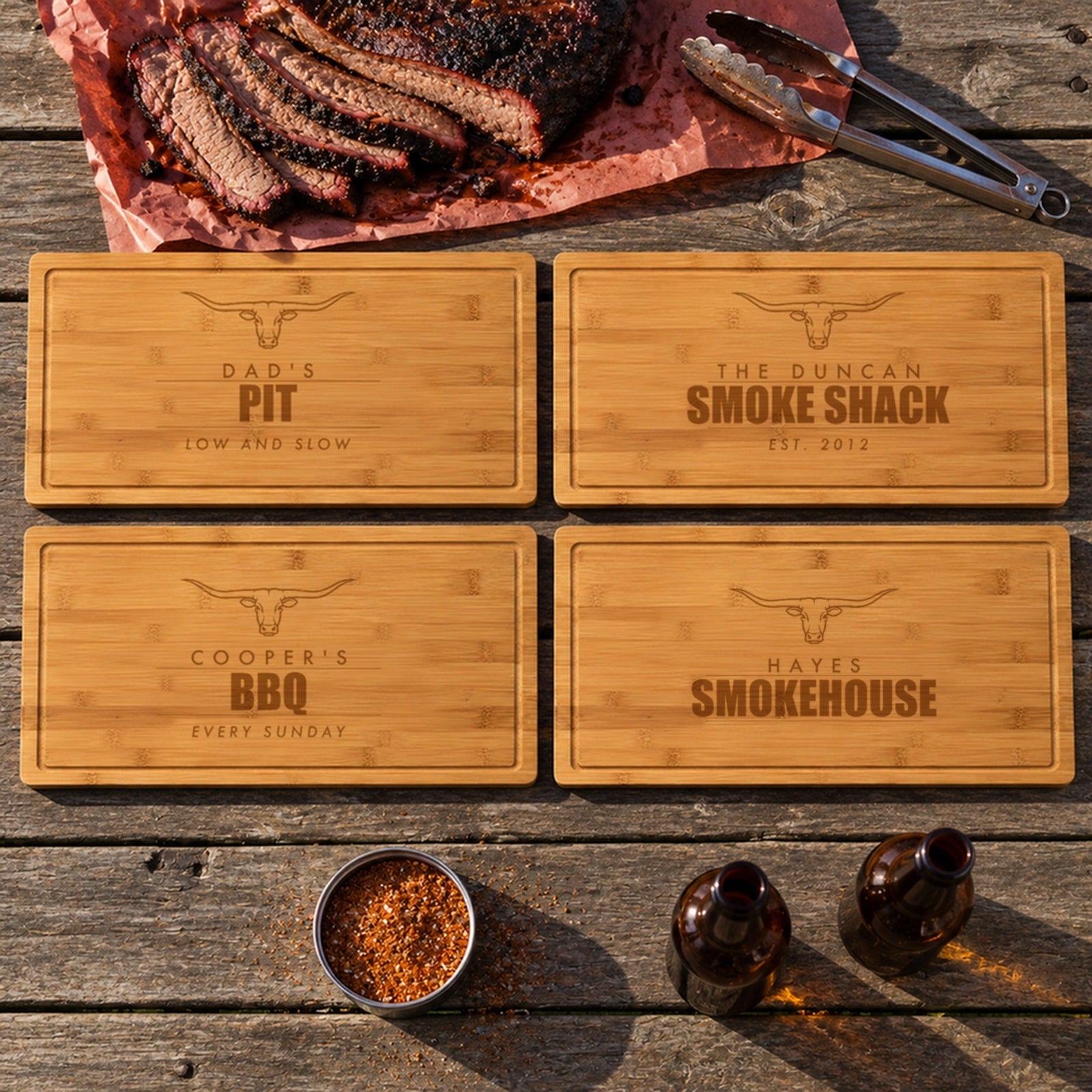 Four engraved BBQ cutting boards on a picnic table with brisket: Dad's Pit, The Duncan Smoke Shack, Cooper's BBQ and Hayes Smokehouse