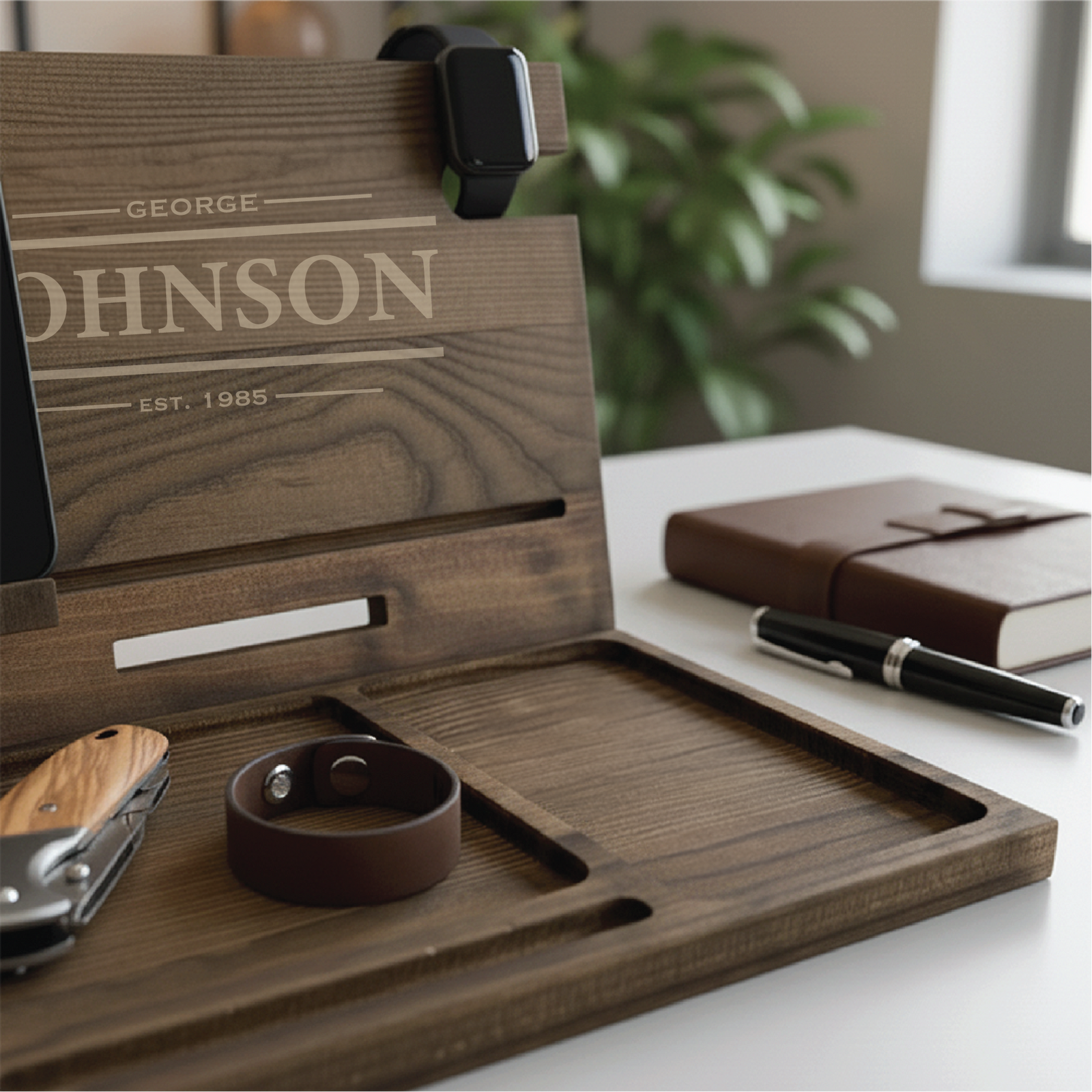 Walnut wood desk organizer with laser-engraved sample personalization reading "GEORGE JOHNSON EST. 1985," featuring compartments for phone, watch, wallet, and keys on a desktop setup