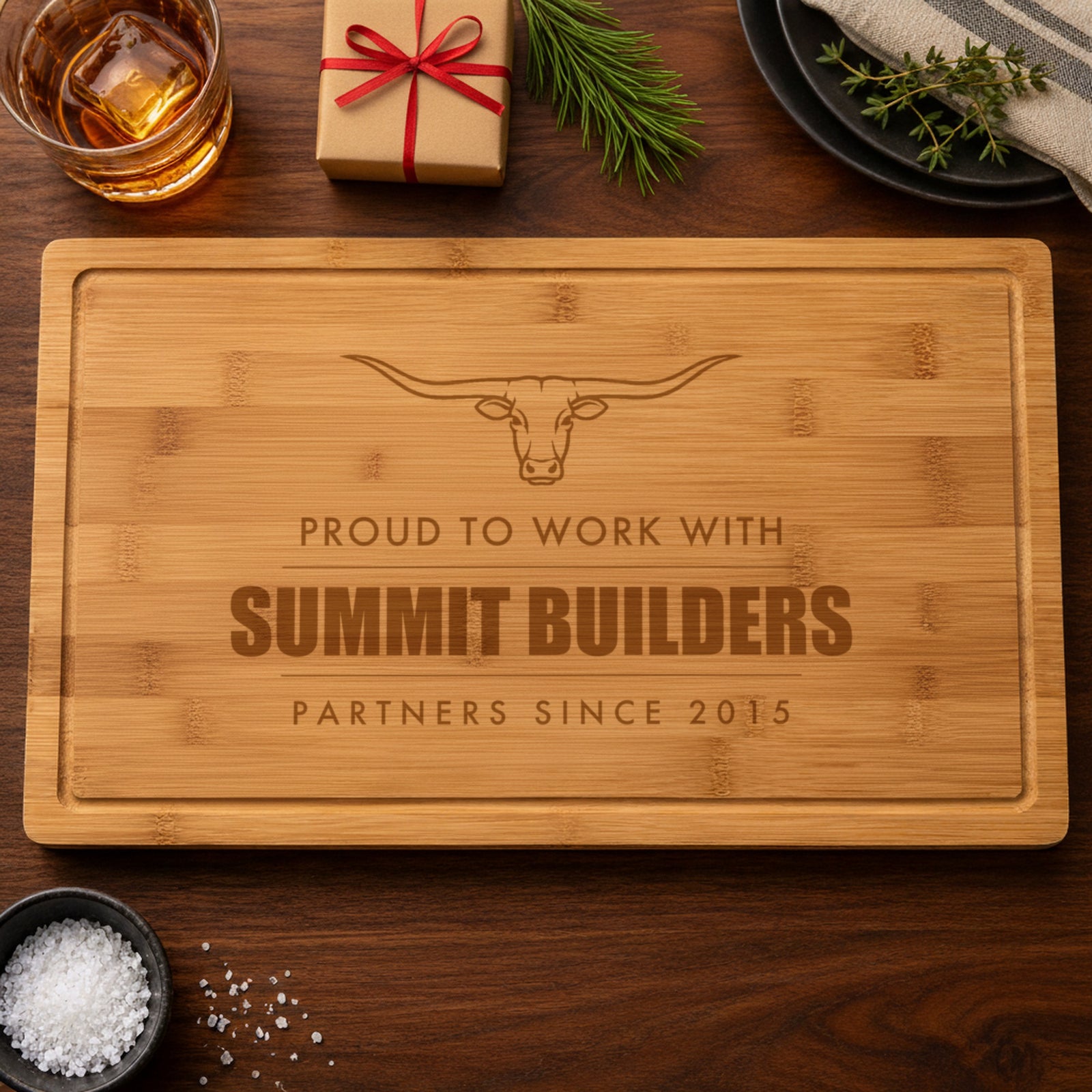 Personalized corporate gift cutting board engraved Proud to Work With, Summit Builders and Partners Since 2015 under a longhorn, beside a wrapped gift