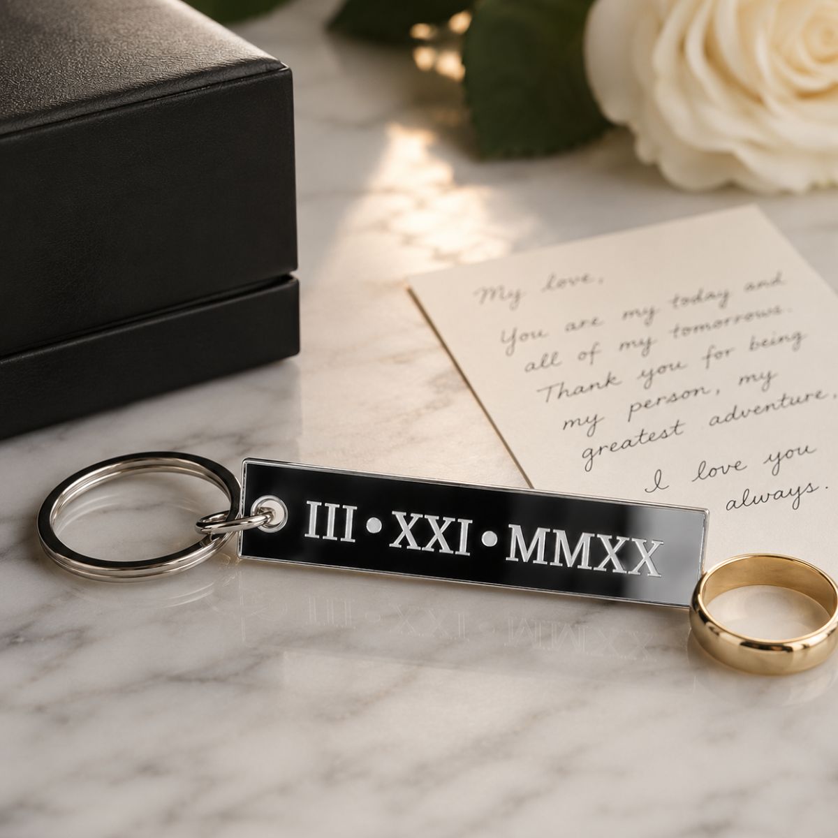 Anniversary Keychain with Roman numeral and year engraving on a marble surface with a ring and card.
