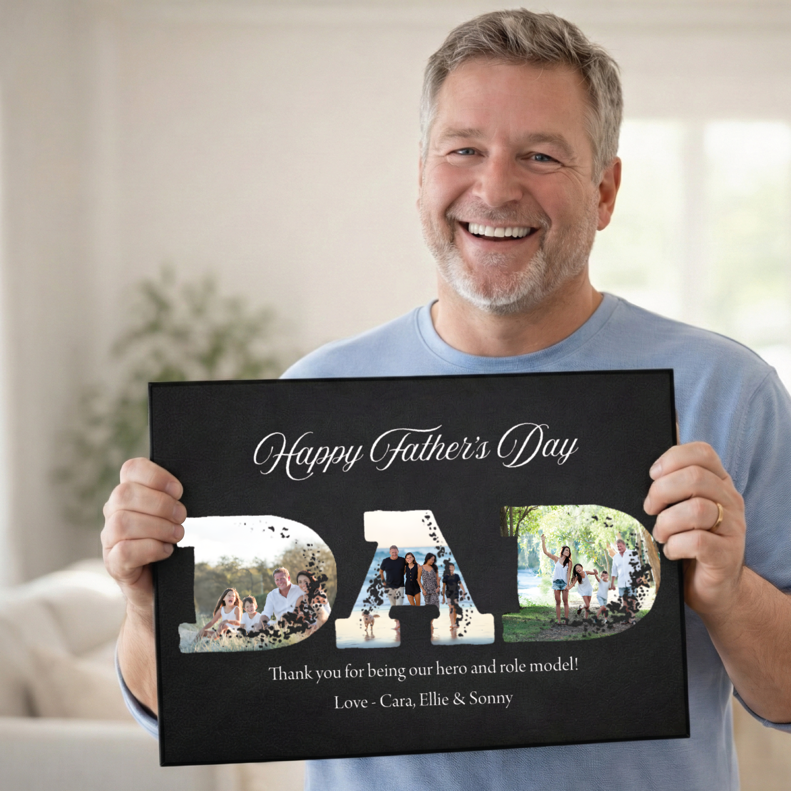 Man holding black canvas displaying "Happy Father's Day DAD" with three family photos integrated into letters, personalized message "Thank you for being our hero and role model! Love - Cara, Ellie & Sonny