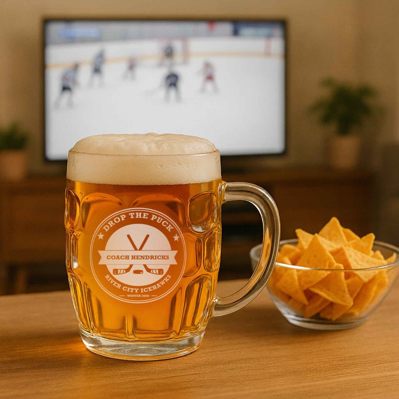 Hockey coach beer stein engraved Drop the Puck for Coach Hendricks of River City Icehawks, on a table with an ice hockey game on TV