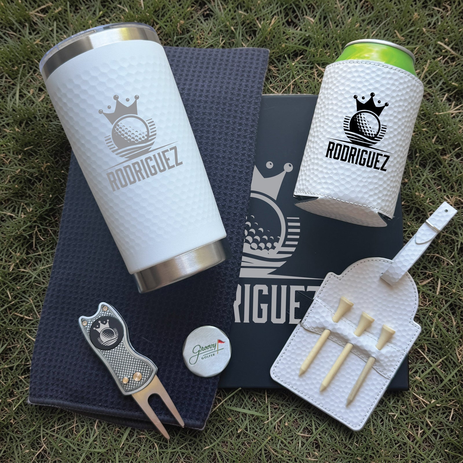 Five-piece personalized golf set with sample engraving "RODRIGUEZ" displayed on white tumbler, can cooler, divot tool, tee holder, and microfiber towel on black gift box