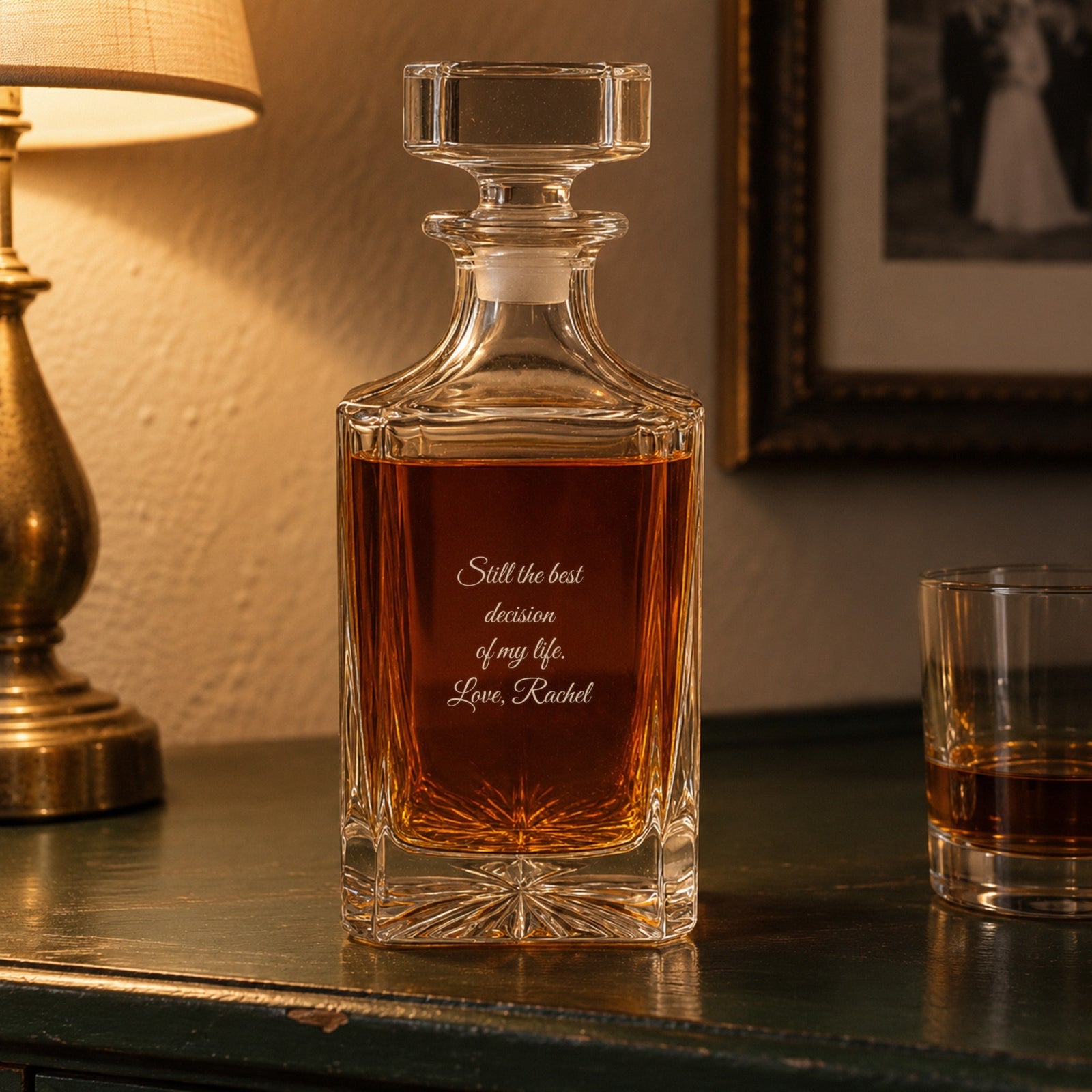 Back of a 15 year anniversary gift for him, the decanter engraved Still the best decision of my life, Love, Rachel, on a sideboard by a lamp