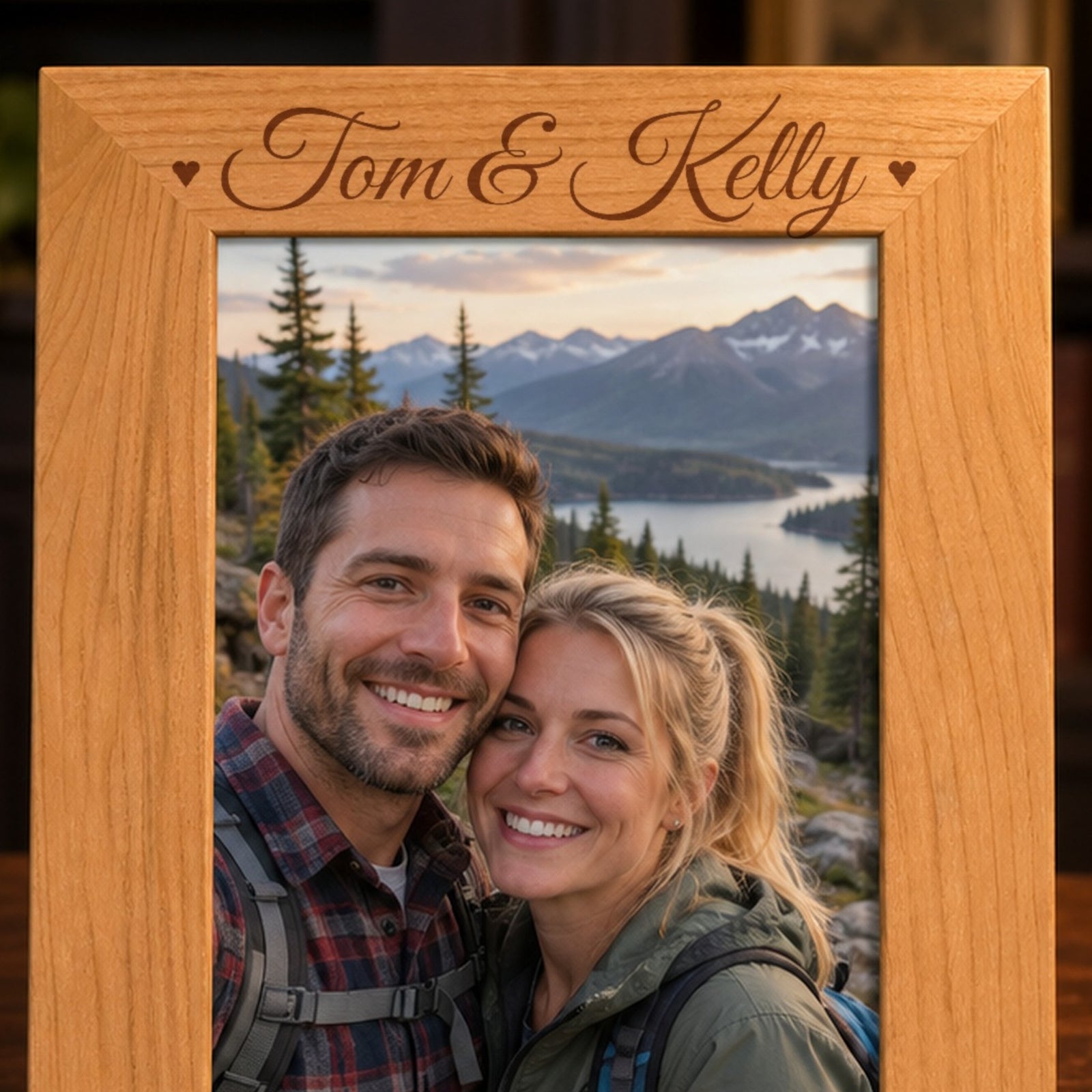 Close-up of the names Tom & Kelly laser engraved in script with two small hearts on the top border of a red alder anniversary picture frame