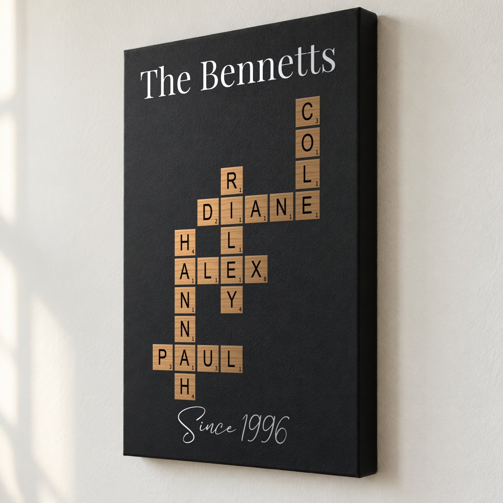 Close angled view of the family crossword wall art showing the 1.5 inch deep edge and wood-tone letter tiles printed flat on black leatherette