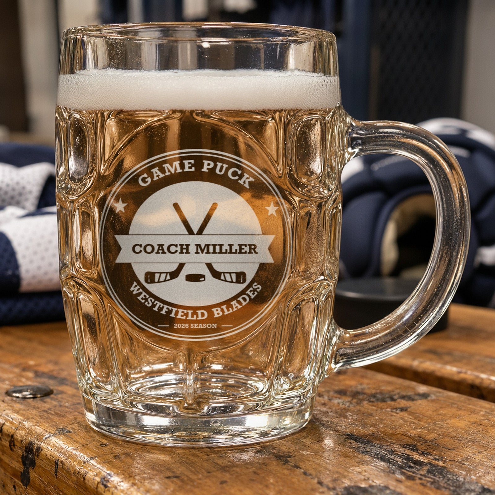 Personalized hockey coach beer stein beside a pair of hockey gloves and a folded jersey, frosted engraving reading Game Puck, Coach Miller and Westfield Blades