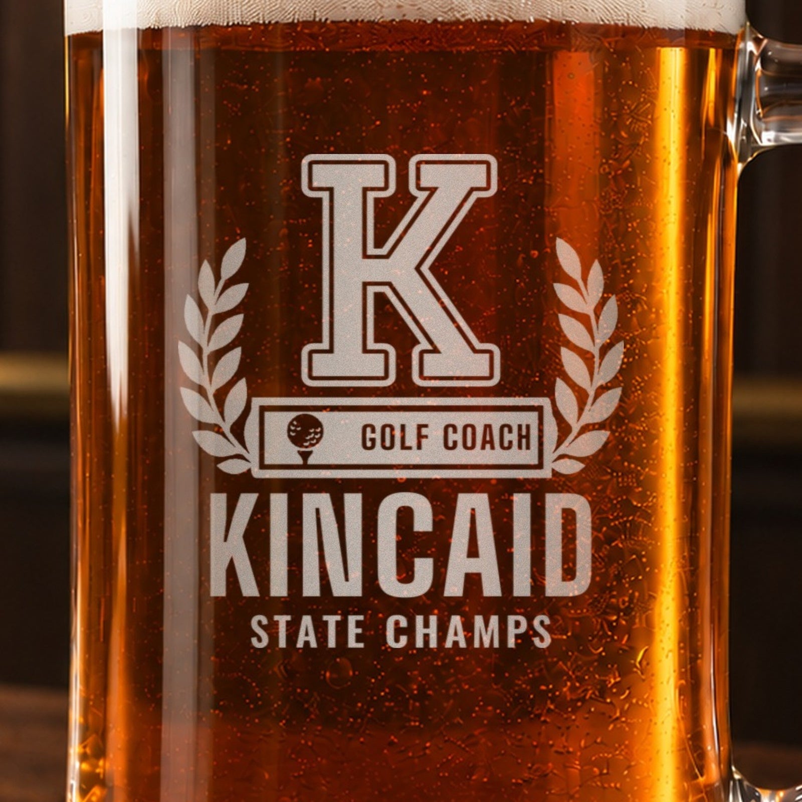 Close-up of the frosted engraving on the golf coach letterman beer stein, a varsity letter with laurel and a golf ball COACH bar: K, Golf Coach, Kincaid, State Champs