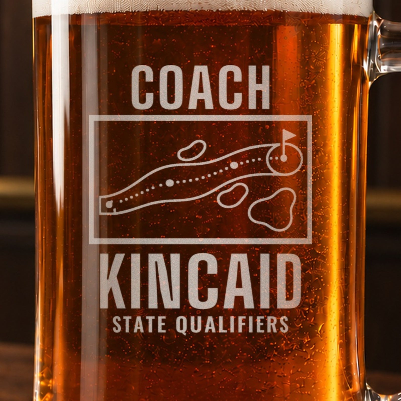 Close-up of the frosted engraving on the golf coach yardage book beer stein, a golf hole map with tee, fairway, bunkers, water and green: Coach, Kincaid, State Qualifiers